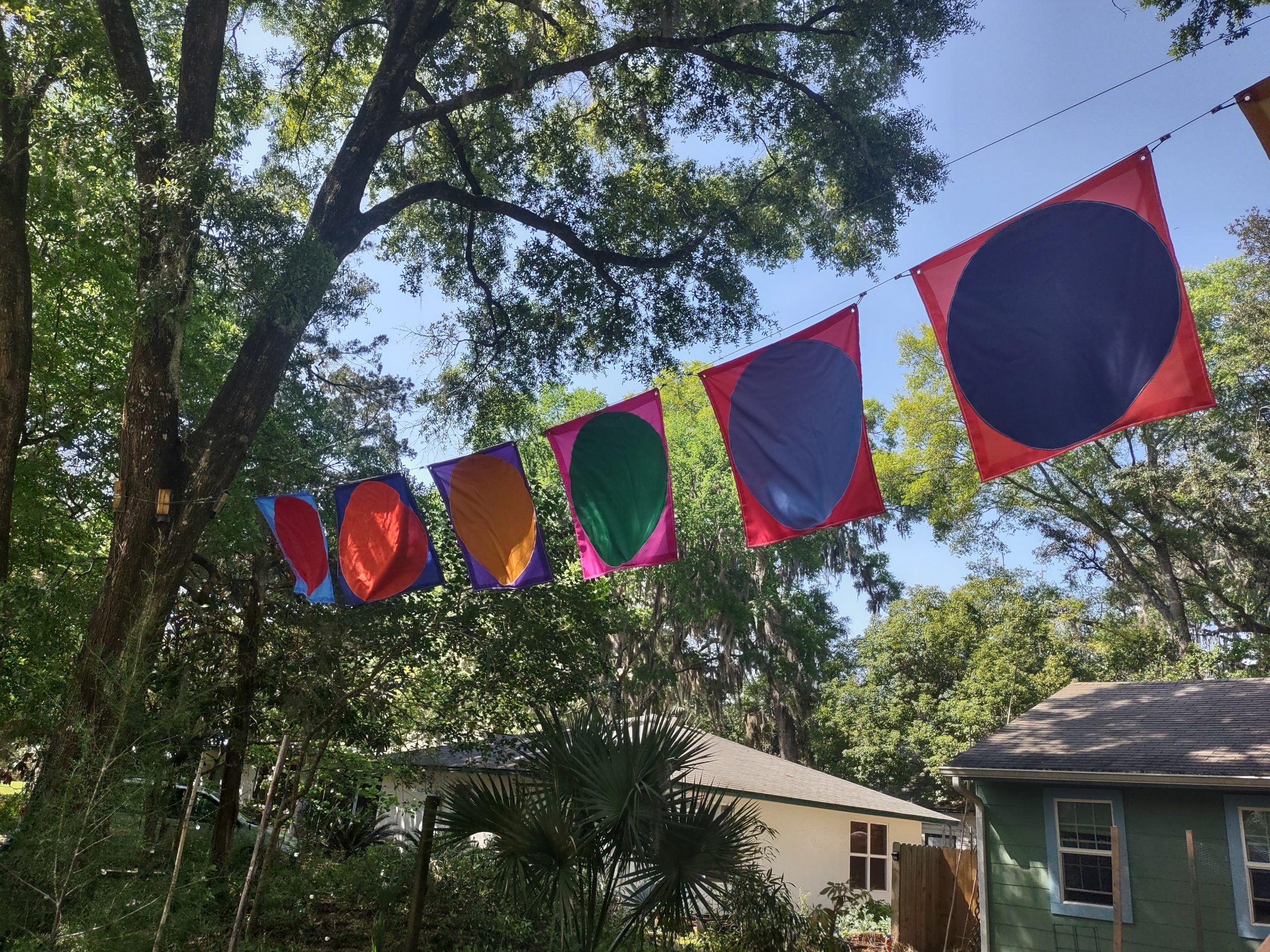 brightly colored square flags with a different color circle filling most of the space in an outdoor setting, all the flags hang side by side on a line