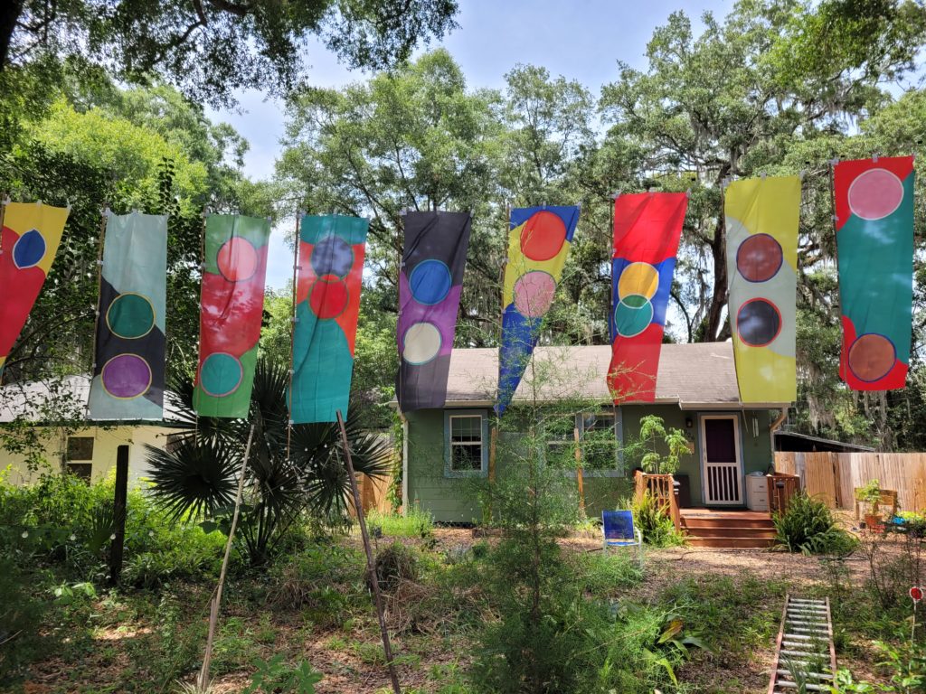 Colorful vertical flags with circles, and wavy spaces hanging in a green space in front of a green house