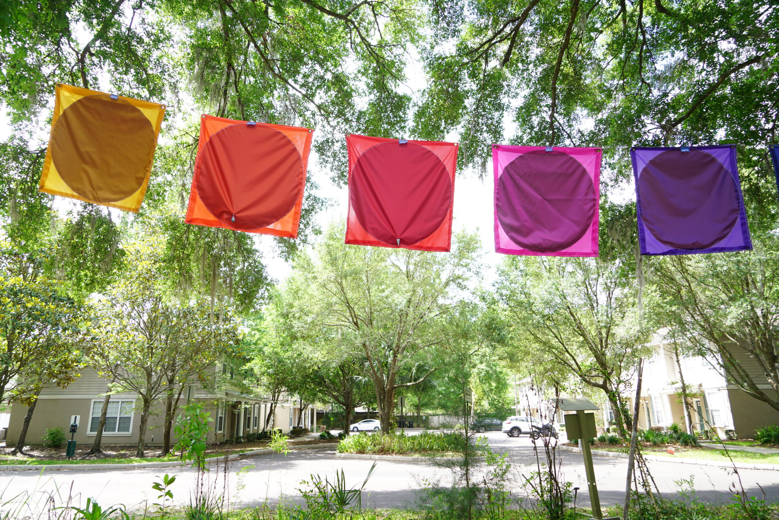 brightly colored square flags with a different color circle filling most of the space in an outdoor setting, all the flags hang side by side on a line