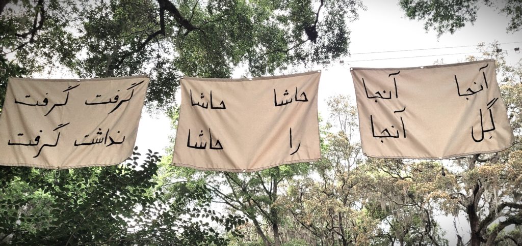 Black Farsi Text on White Fabric Flags hanging outdoors in a green space